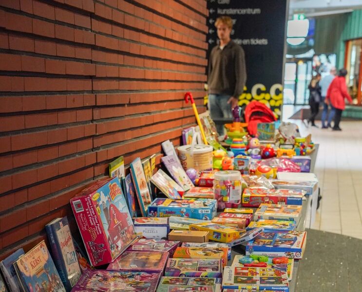 Lange tafel met tweedehands speelgoed, spellen en kinderboeken voor een Sintswap bij Cpunt, opgesteld langs een bakstenen muur.